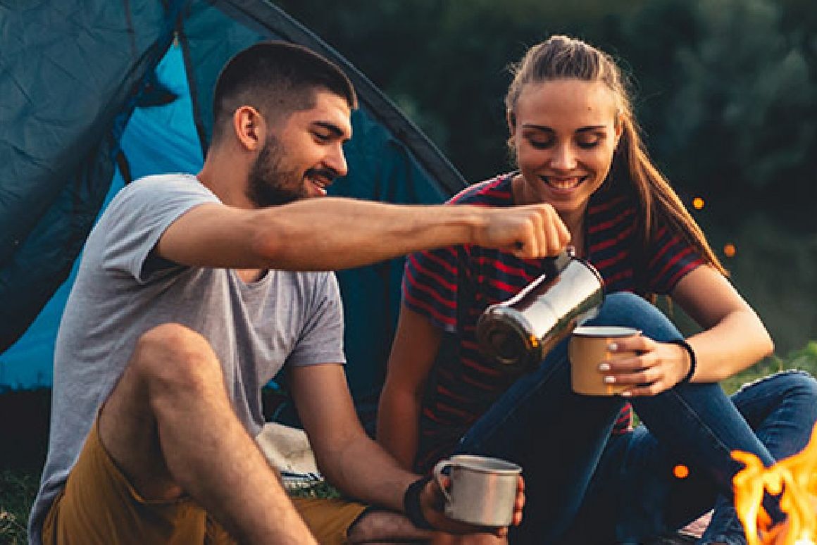 Mann schüttet Frau etwas in Tasse beim Camping